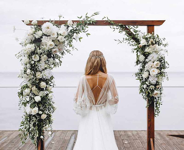 Braut vor Traubogen. Traubogen mit weißen Blumen geschmückt.